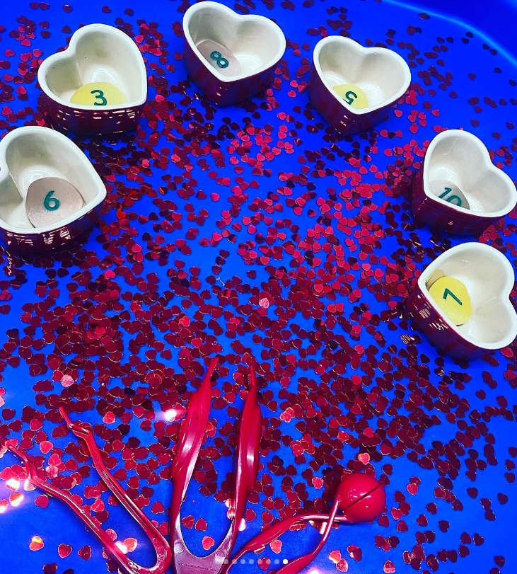 A creative Tuff Tray setup with Valentine-themed sensory bins and educational activities.