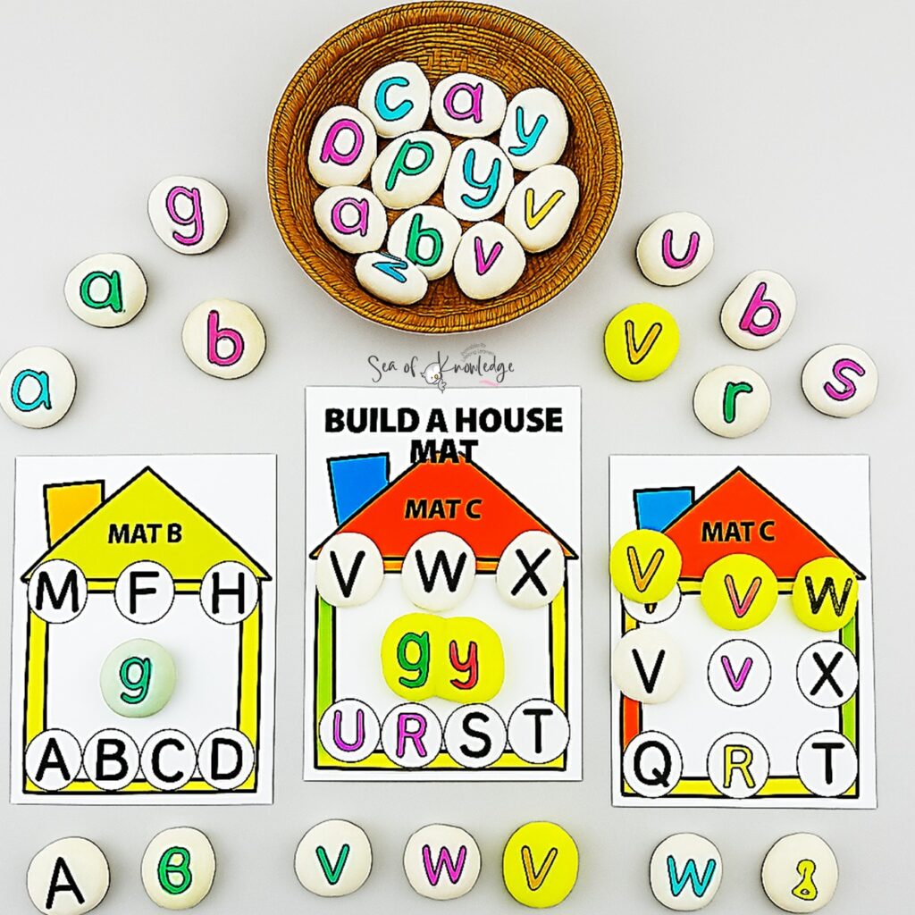 Child’s hands placing colorful letter stones onto a Build a House alphabet mat for matching game.