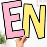 Pink E and yellow N letter cutouts with bold black outlines held in front of a classroom wall.