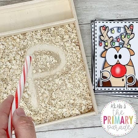 Candy cane tracing a letter in an oat tray beside a reindeer alphabet card